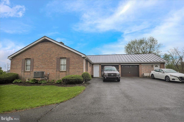 view of side of property featuring brick siding, a garage, cooling unit, a yard, and driveway