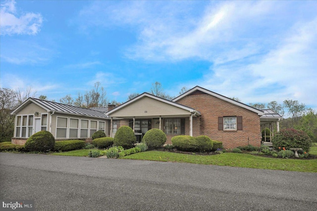 ranch-style home featuring brick siding, metal roof, a sunroom, and a standing seam roof