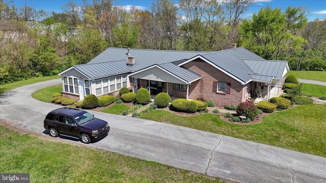 view of front of home featuring aphalt driveway, a front yard, a standing seam roof, brick siding, and metal roof