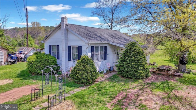 view of side of home with a lawn, a shingled roof, and a chimney