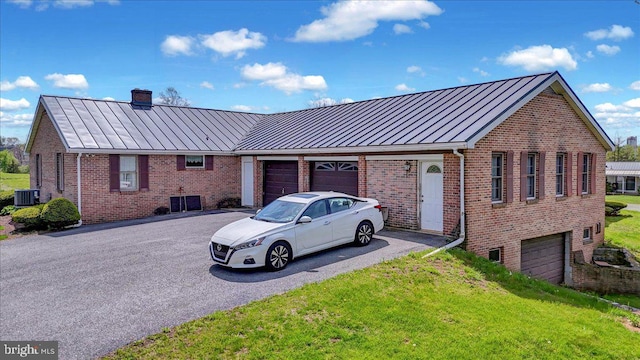 view of front facade with a standing seam roof, a chimney, central AC unit, brick siding, and aphalt driveway