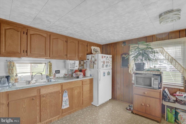 kitchen with wooden walls, a sink, light countertops, freestanding refrigerator, and stainless steel microwave