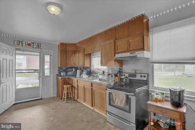 kitchen featuring decorative backsplash, under cabinet range hood, brown cabinets, and stainless steel electric range oven