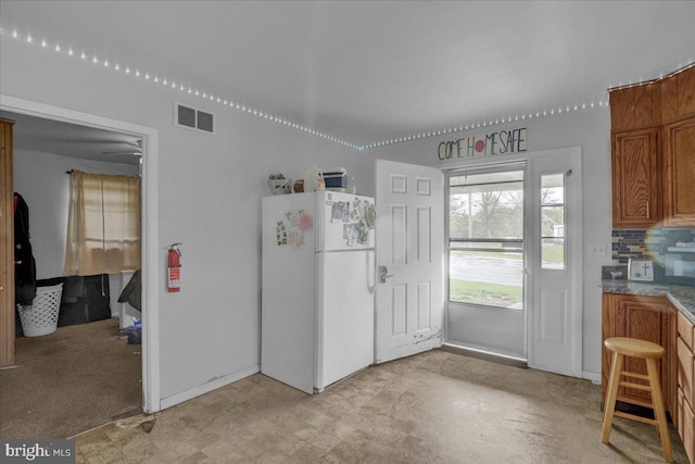 kitchen with brown cabinetry, freestanding refrigerator, baseboards, light floors, and visible vents