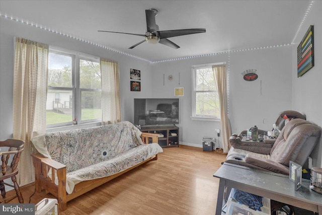 living area featuring a ceiling fan, baseboards, and light wood finished floors