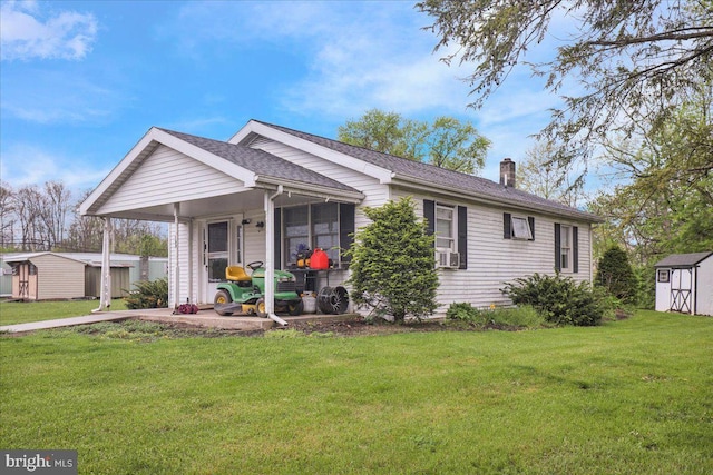 single story home with a chimney, roof with shingles, an outbuilding, a shed, and a front lawn