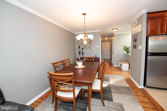 dining area with an inviting chandelier, ornamental molding, light wood-style flooring, and visible vents