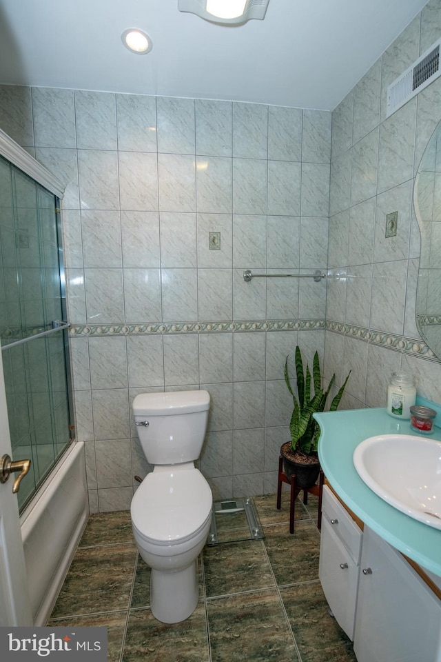 bathroom with tile walls, combined bath / shower with glass door, visible vents, and vanity