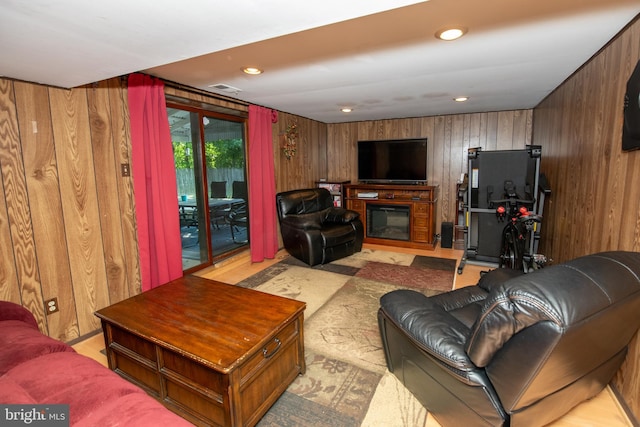 living area featuring wooden walls, recessed lighting, visible vents, and a glass covered fireplace