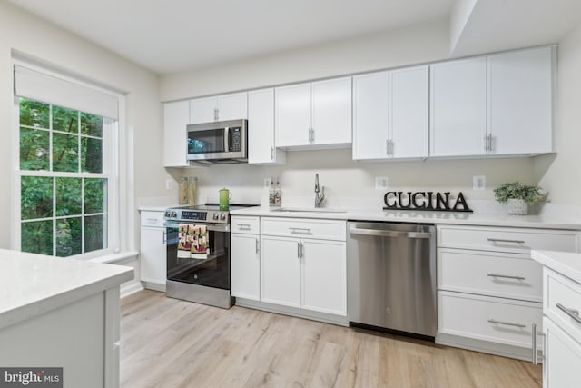 kitchen featuring appliances with stainless steel finishes, a sink, light countertops, white cabinets, and light wood-type flooring