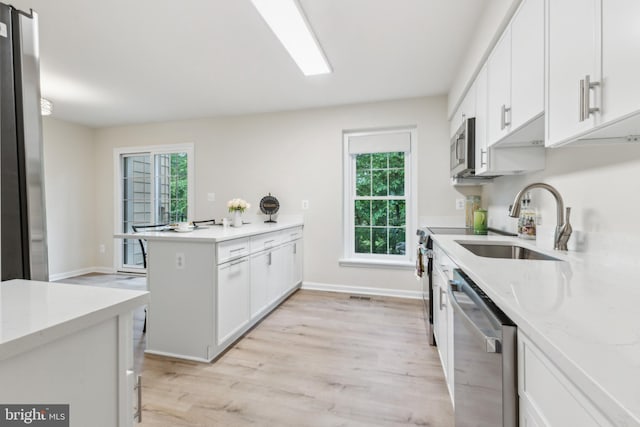 kitchen featuring stainless steel appliances, a sink, a peninsula, light wood-style floors, and healthy amount of natural light
