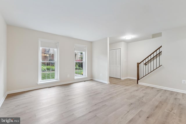 unfurnished living room with light wood-style flooring, baseboards, and stairs