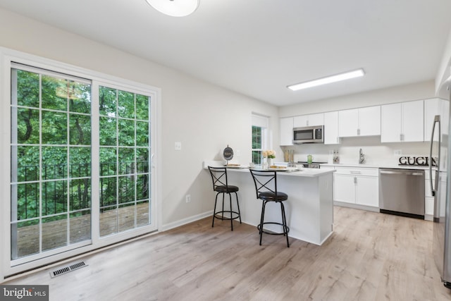 kitchen with stainless steel appliances, light wood-style flooring, white cabinets, and a peninsula