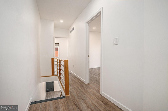 corridor featuring baseboards, visible vents, wood finished floors, and an upstairs landing
