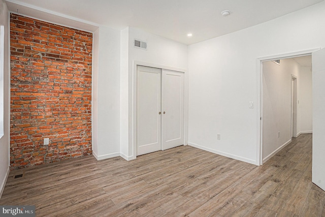 unfurnished bedroom with visible vents, a closet, wood finished floors, brick wall, and baseboards