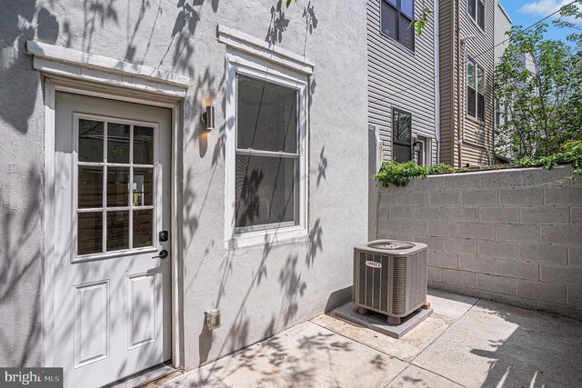 entrance to property with stucco siding, a patio area, central AC, and fence