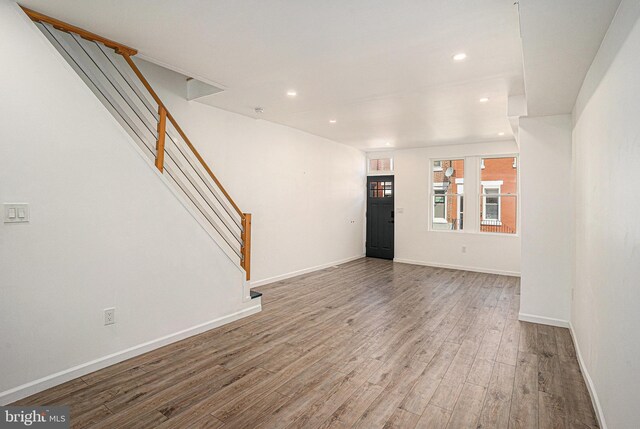 unfurnished living room with recessed lighting, baseboards, wood finished floors, and stairway