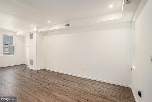 empty room featuring dark wood-style flooring, baseboards, and visible vents