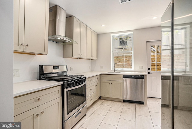 kitchen featuring wall chimney range hood, appliances with stainless steel finishes, a sink, and light countertops
