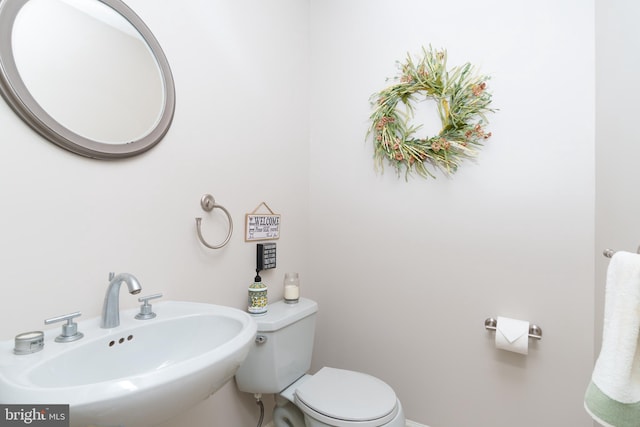 half bath featuring toilet, baseboards, and a sink