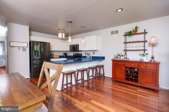 kitchen featuring a peninsula, wood finished floors, white cabinets, visible vents, and black appliances