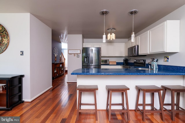 kitchen with a peninsula, dark countertops, white cabinets, dark wood-style flooring, and appliances with stainless steel finishes