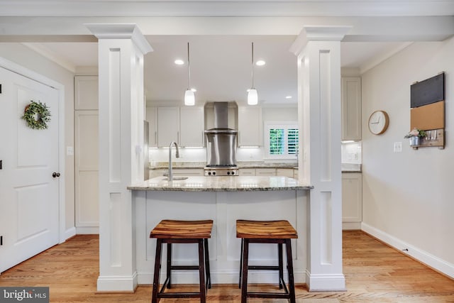 3207 19th St N, Arlington, VA 22201 - kitchen featuring wall chimney range hood, decorative columns, light wood-style flooring, a kitchen bar, and recessed lighting