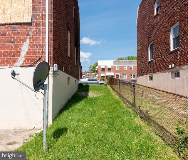 view of side of home featuring a yard, brick siding, and fence