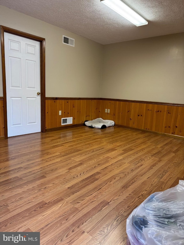 empty room featuring a textured ceiling, visible vents, and light wood finished floors