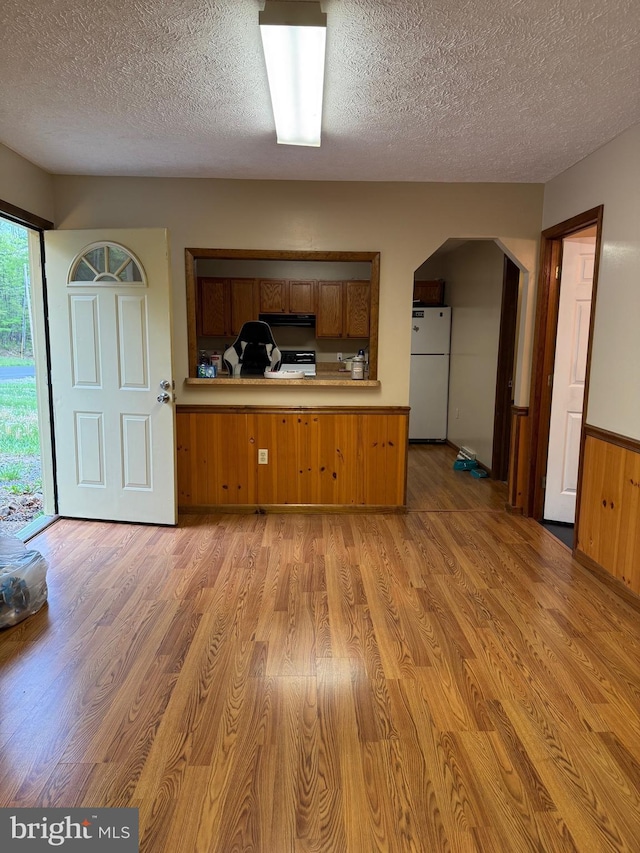 kitchen featuring arched walkways, a textured ceiling, brown cabinetry, light wood-style flooring, and freestanding refrigerator