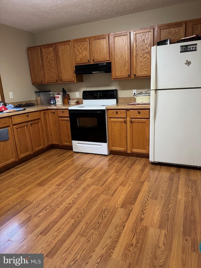 kitchen featuring freestanding refrigerator, range with electric stovetop, brown cabinetry, and under cabinet range hood