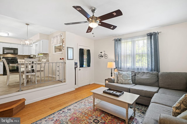 living area with baseboards, a ceiling fan, and light wood finished floors