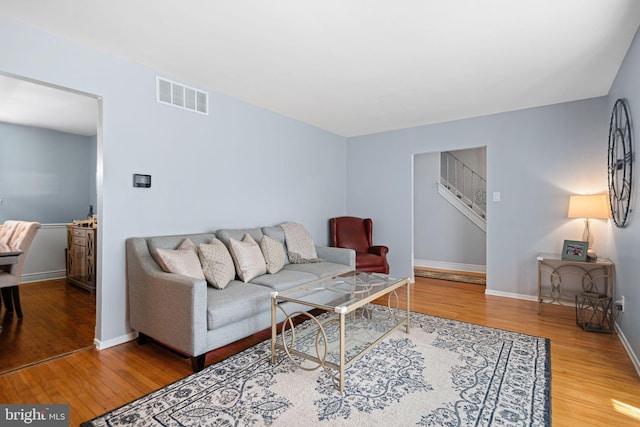 living room with stairway, baseboards, wood finished floors, and visible vents