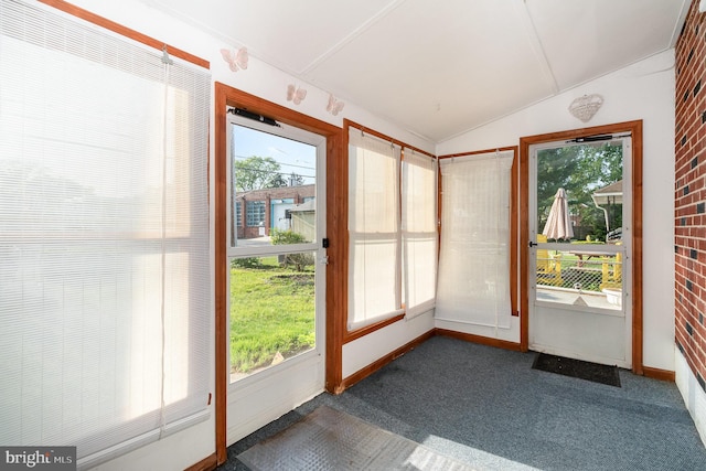 unfurnished sunroom featuring carpet floors, baseboards, vaulted ceiling, and a healthy amount of sunlight