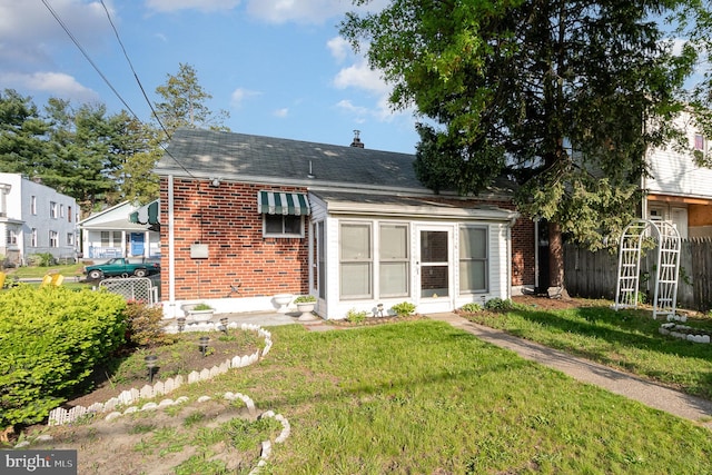 rear view of property with fence, a shingled roof, a yard, and brick siding