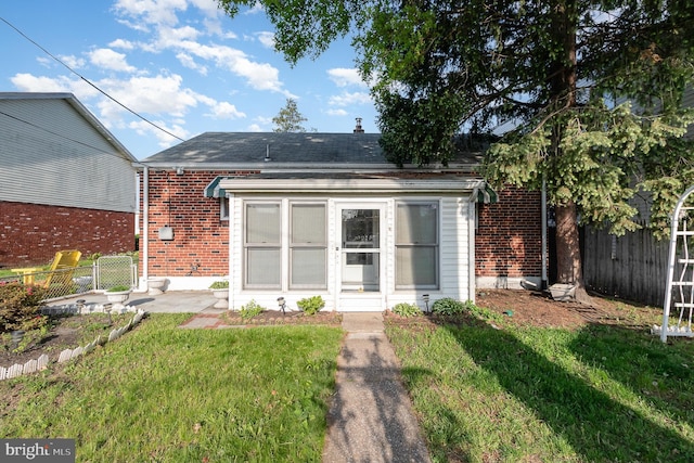back of property with brick siding, a shingled roof, a lawn, and fence