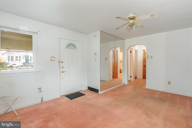 foyer entrance with arched walkways, a ceiling fan, light colored carpet, and baseboards