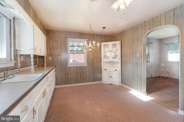kitchen with a sink, arched walkways, white cabinets, and light carpet