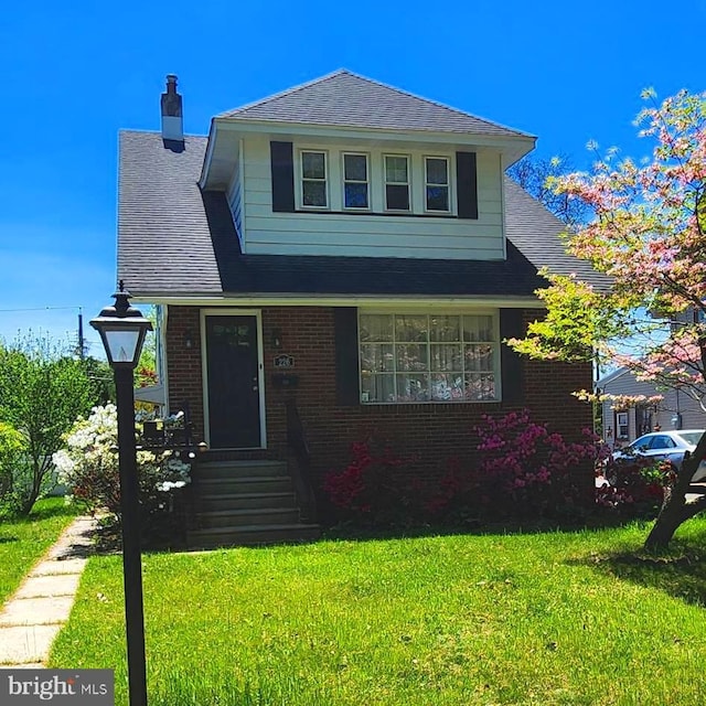 bungalow-style house featuring a shingled roof, a front lawn, brick siding, entry steps, and a chimney