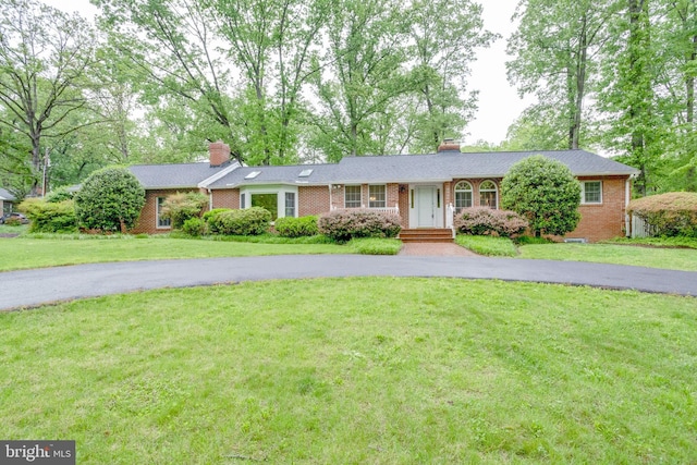 single story home featuring a chimney, driveway, brick siding, and a front lawn