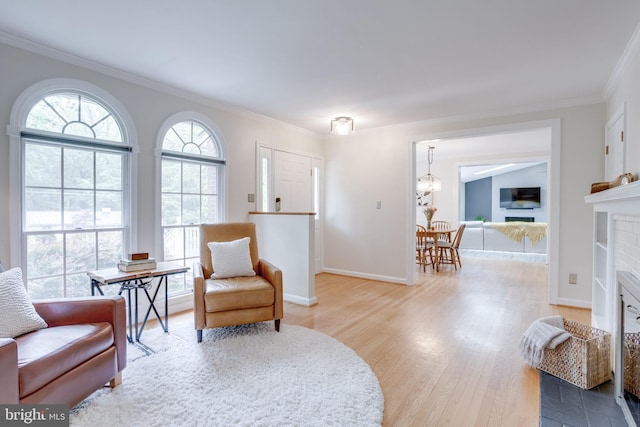 sitting room featuring a fireplace with flush hearth, light wood-style floors, ornamental molding, a chandelier, and baseboards
