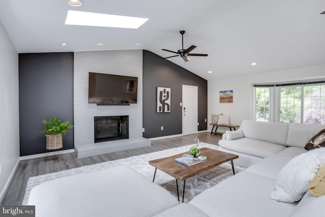 living room featuring wood finished floors, vaulted ceiling, a fireplace, baseboards, and a skylight