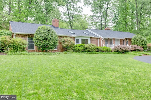 ranch-style home featuring a chimney, brick siding, a front lawn, and roof with shingles