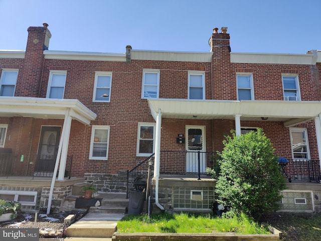 townhome / multi-family property featuring covered porch, brick siding, and a chimney