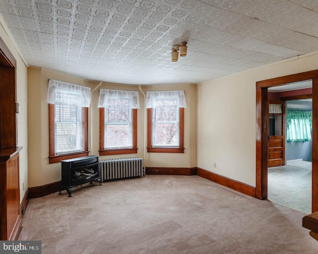 empty room featuring an ornate ceiling, baseboards, radiator heating unit, a wood stove, and carpet floors