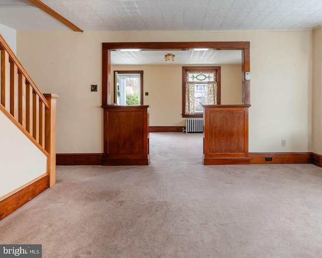 unfurnished living room featuring stairs, carpet, baseboards, and radiator heating unit
