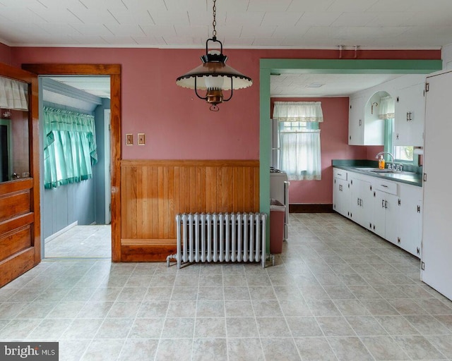 kitchen featuring a sink, wood walls, radiator, a wainscoted wall, and white cabinetry