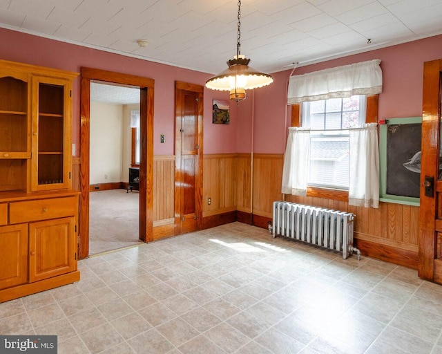 unfurnished dining area with a wainscoted wall, wooden walls, and radiator heating unit