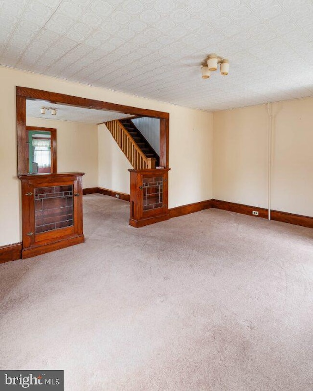 unfurnished living room with carpet, baseboards, and stairs