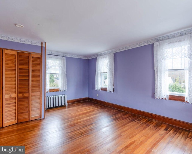 unfurnished bedroom with radiator, a closet, baseboards, and hardwood / wood-style floors
